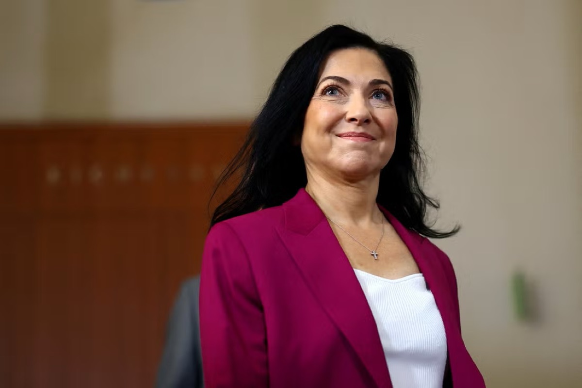 Katherina Reiche smiling, wearing a magenta jacket, in a wood-panelled interior