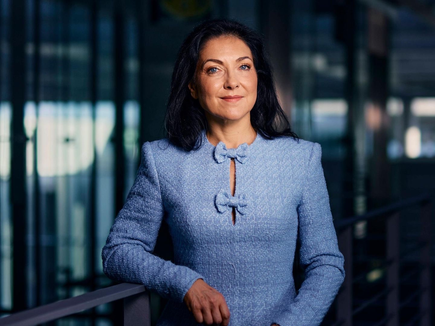 Katherina Reiche in a light blue jacket standing in front of a modern glass building