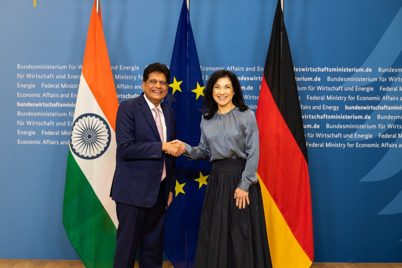 Katherina Reiche shaking hands with an Indian minister in front of Indian, EU and German flags at the ministry