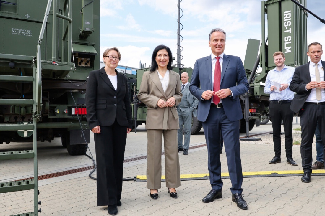 Katherina Reiche with officials during an outdoor site visit beside military vehicles