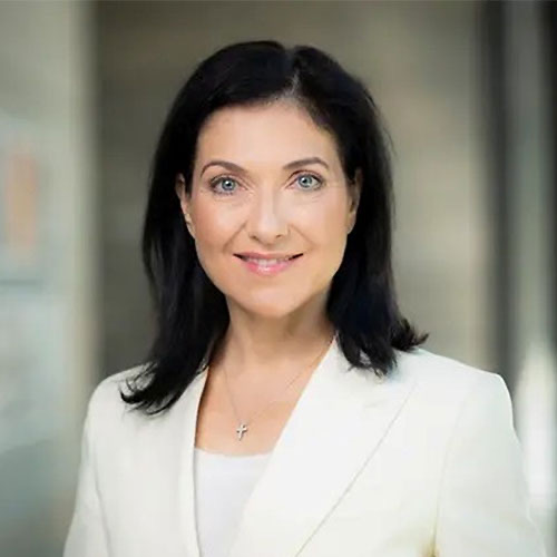 Portrait of Katherina Reiche smiling, in a white blazer against a neutral background