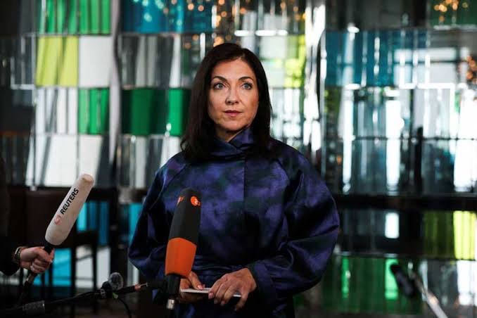 Katherina Reiche speaking to the press at microphones in front of a modern industrial building