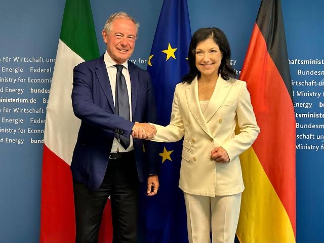 Katherina Reiche shaking hands with an Italian counterpart in front of Italian, EU and German flags